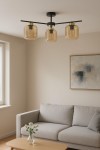 Lampa sufitowa Iga z trzema kloszami E27 w kolorze czarnym i bursztynowym. Klosze mają prostokątny kształt z widocznymi żarówkami. Lampa zamontowana na suficie, w jasnym wnętrzu z kanapą i stołem.