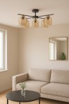 Lampa sufitowa Iga w kolorze czarnym z pięcioma bursztynowymi kloszami E27. Ujęcie frontalne, zamontowana na suficie. Otoczenie jasne, z kanapą i stolikiem kawowym w tle. Klosze mają zaokrąglony kształt, a lampa prezentuje nowoczesny design.