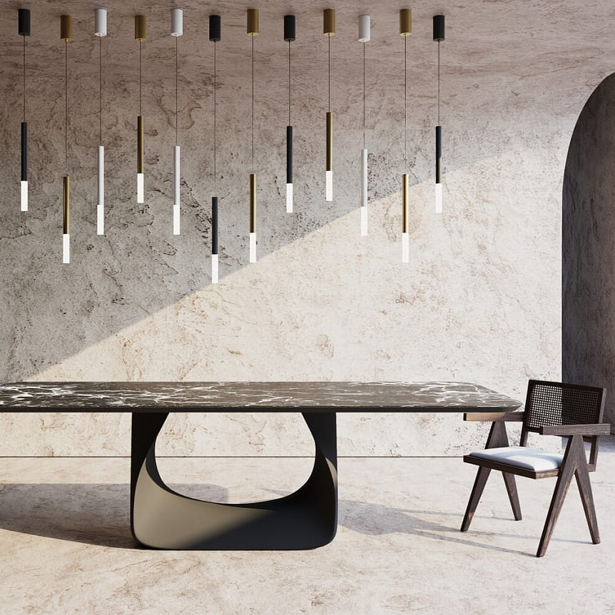Lampa wisząca LED Pro Shade w białym kolorze, z sześcioma smukłymi, cylindrycznymi kloszami w różnych kolorach (czarnym, białym, złotym) zwisającymi z sufitu. Ujęcie frontalne, z minimalistycznym stołem i krzesłem w tle, na jasnym, teksturowanym tle.