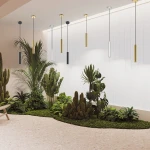Lampa wisząca Pro Focus 1xGU10 w złotym kolorze, cylindryczny kształt, zawieszona na czarnym kablu. W tle widoczna dekoracja roślinna z palmami i kaktusami, na jasnym tle. Lampa w aranżacji nowoczesnej przestrzeni.