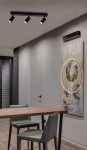 Monti lampa sufitowa w kolorze czarnym z trzema reflektorami GU10. Ujęcie z góry, zamontowana na suficie nad drewnianym stołem i krzesłami, w nowoczesnym wnętrzu z dekoracyjnym obrazem na ścianie.