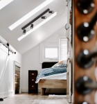 Czarna lampa sufitowa Monti z czterema spotami GU10, zamontowana na skosie w jasnym wnętrzu. Widoczne elementy to drewniane łóżko z niebiesko-białą pościelą oraz szafa i komoda w tle. Oświetlenie skierowane w różnych kierunkach.