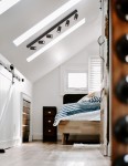 Czarna lampa sufitowa Monti z sześcioma reflektorami GU10, zamontowana na skosie pod sufitem w jasnym pomieszczeniu. Reflektory są skierowane w różne strony, oświetlając przestrzeń nad łóżkiem z pościelą w paski.