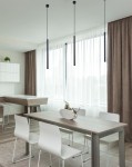 Lampa wisząca Gelato 1xG9 w kolorze czarnym, o smukłej, prostokątnej formie, zawieszona na długich przewodach. Umieszczona w nowoczesnym wnętrzu, nad drewnianym stołem, z białymi krzesłami w tle. Jasne zasłony i stonowane kolory otoczenia.