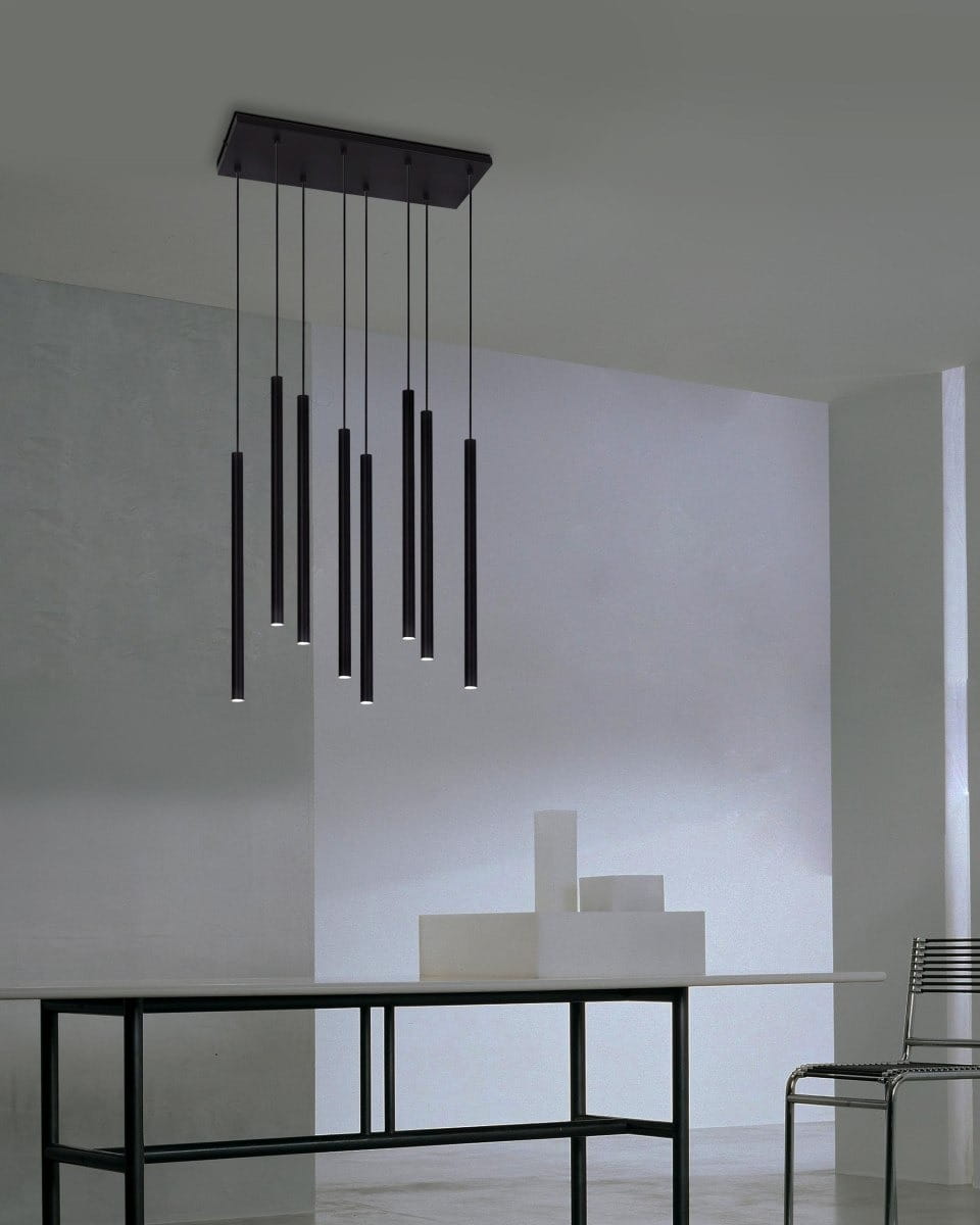 Lampa wisząca Gelato z ośmioma oprawami G9 w kolorze czarnym. Posiada prostokątny sufitowy uchwyt, z którego zwisają długie, cylindryczne klosze. Umieszczona nad stołem w nowoczesnym wnętrzu, na jasnym tle ściany.