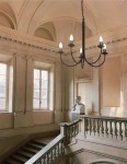 Czarny żyrandol świecznikowy Haris z pięcioma oprawkami E14, wiszący na łańcuchu. Produkt umieszczony w eleganckim wnętrzu z monumentalnymi schodami i klasycznymi detalami architektonicznymi.