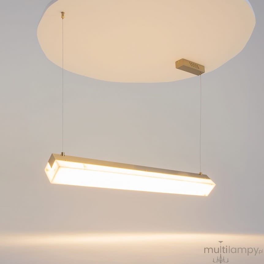 Lampa wisząca Petra LED w kolorze mosiądzu, o prostokątnym kształcie, z białym kloszem. Zawieszona na cienkich linkach, emitująca ciepłe światło (3000K). Montaż sufitowy, minimalistyczny design, idealna do nowoczesnych wnętrz.