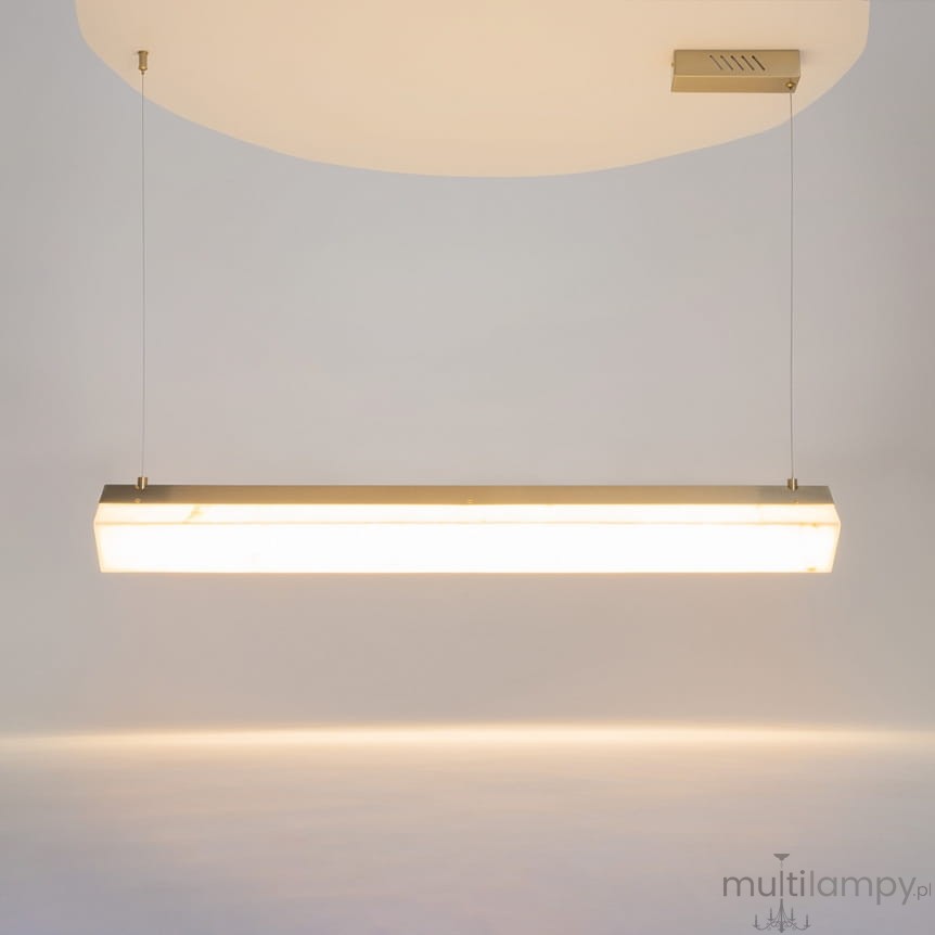 Lampa wisząca LED Petra o mocy 35W, barwie światła 3000K, w mosiężnej obudowie. Prosty, prostokątny kształt, zawieszona na cienkich linkach, emitująca ciepłe światło. Tło jasne, minimalistyczne.