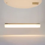 Lampa wisząca LED Petra o mocy 35W, barwie światła 3000K, w mosiężnej obudowie. Prosty, prostokątny kształt, zawieszona na cienkich linkach, emitująca ciepłe światło. Tło jasne, minimalistyczne.