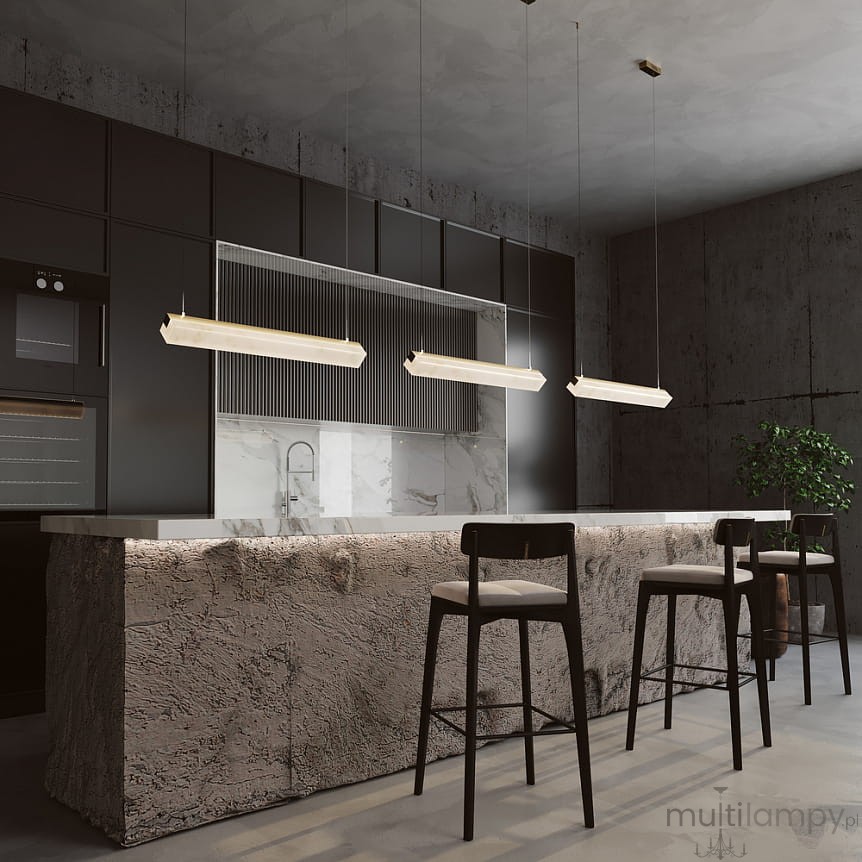 Lampa wisząca LED Petra o mocy 35W i temperaturze barwowej 3000K w kolorze mosiądzu, zawieszona nad stołem barowym w nowoczesnej kuchni. Otoczenie z betonowymi ścianami i ciemnymi meblami, w tle widoczne krzesła i roślina.