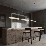Lampa wisząca LED Petra o mocy 35W i temperaturze barwowej 3000K w kolorze mosiądzu, zawieszona nad stołem barowym w nowoczesnej kuchni. Otoczenie z betonowymi ścianami i ciemnymi meblami, w tle widoczne krzesła i roślina.