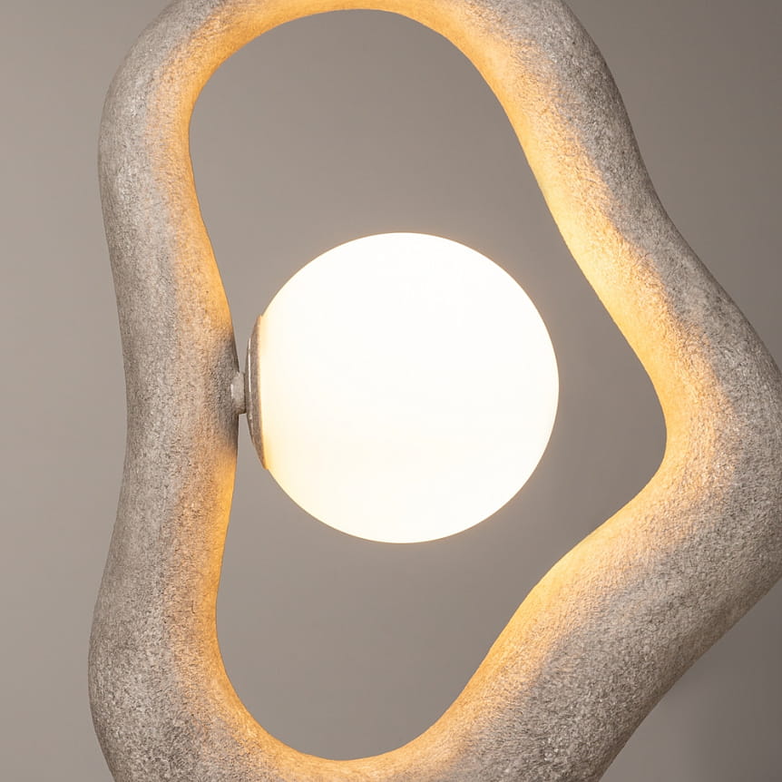 Lampa wisząca Opus w kolorze szarym, z okrągłą, mleczną żarówką G9. Oryginalny, organiczny kształt z teksturą przypominającą beton, z delikatnym podświetleniem. Ujęcie zbliżone na detal lampy, podkreślające fakturę i kształt.