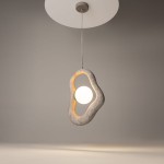 Lampa wisząca Opus w kolorze szarym z jednym źródłem światła G9. Owalny, teksturowany klosz z wycięciem, w którym umieszczona jest okrągła żarówka, zawieszona na cienkim przewodzie. Tło jednolite, szare.