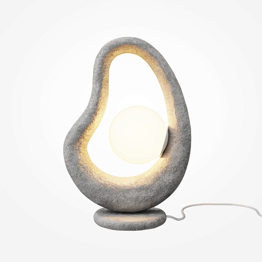 Lampa stołowa Opus w kolorze szarym z jedną żarówką G9. Ma organiczny kształt z wycięciem, w którym umieszczona jest okrągła, mleczna kula. Stoi na okrągłej podstawie, z białym kablem zasilającym. Tło jest jasne i jednolite.