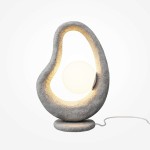 Lampa stołowa Opus w kolorze szarym z jedną żarówką G9. Ma organiczny kształt z wycięciem, w którym umieszczona jest okrągła, mleczna kula. Stoi na okrągłej podstawie, z białym kablem zasilającym. Tło jest jasne i jednolite.
