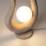 Lampa stołowa Opus w kolorze szarym z podstawką w kształcie organicznej figury, z okrągłą, białą żarówką G9 umieszczoną w jej wnętrzu. Produkt jest widoczny z boku, na jednolitym tle.