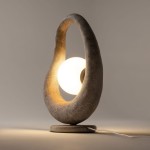 Szara lampa stołowa Opus MOD380TL-01GR z okrągłym kloszem, umieszczona w oprawie o organicznym kształcie. Ujęcie z boku, ukazujące podświetlenie oraz detalowe wykończenie materiału. Kabel zasilający widoczny u podstawy.