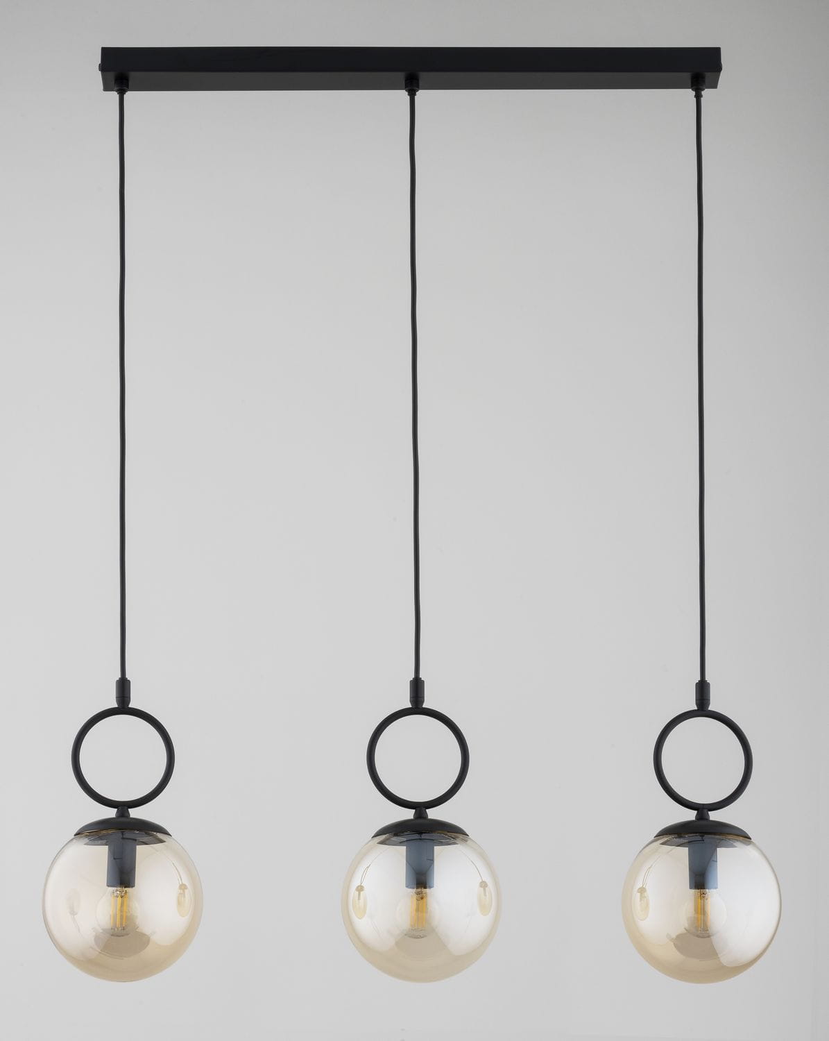Lampa wisząca Sitro z trzema kulistymi kloszami w bursztynowym kolorze, zawieszona na czarnej listwie. Klosze mają metalowe uchwyty w formie pierścieni, a całość prezentuje nowoczesny, minimalistyczny styl.