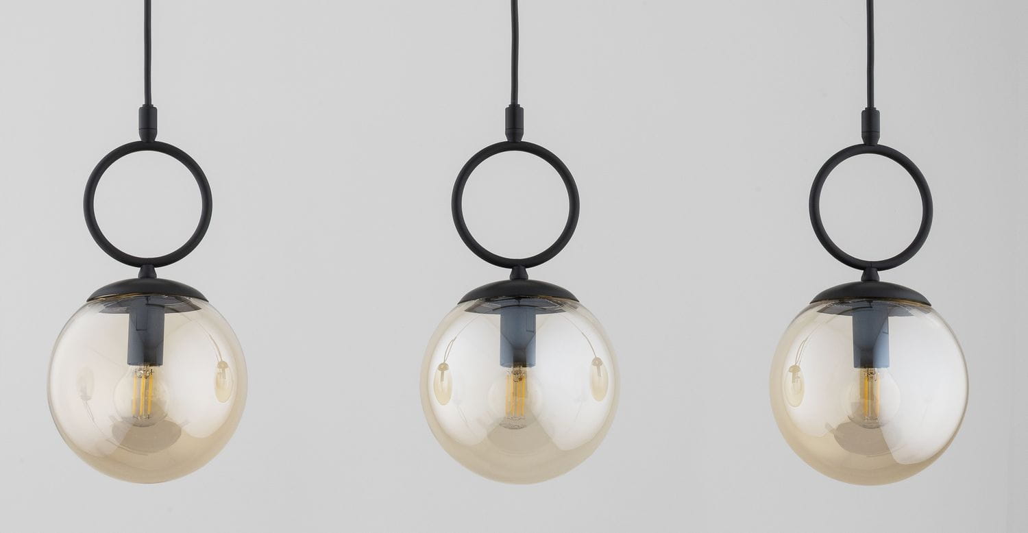 Lampa wisząca Sitro z trzema kulistymi kloszami w kolorze bursztynowym, zawieszona na czarnych linkach. Każdy klosz ma metalowy pierścień oraz miejsce na żarówkę E14, tworząc nowoczesny wygląd. Tło jasne, jednolite.