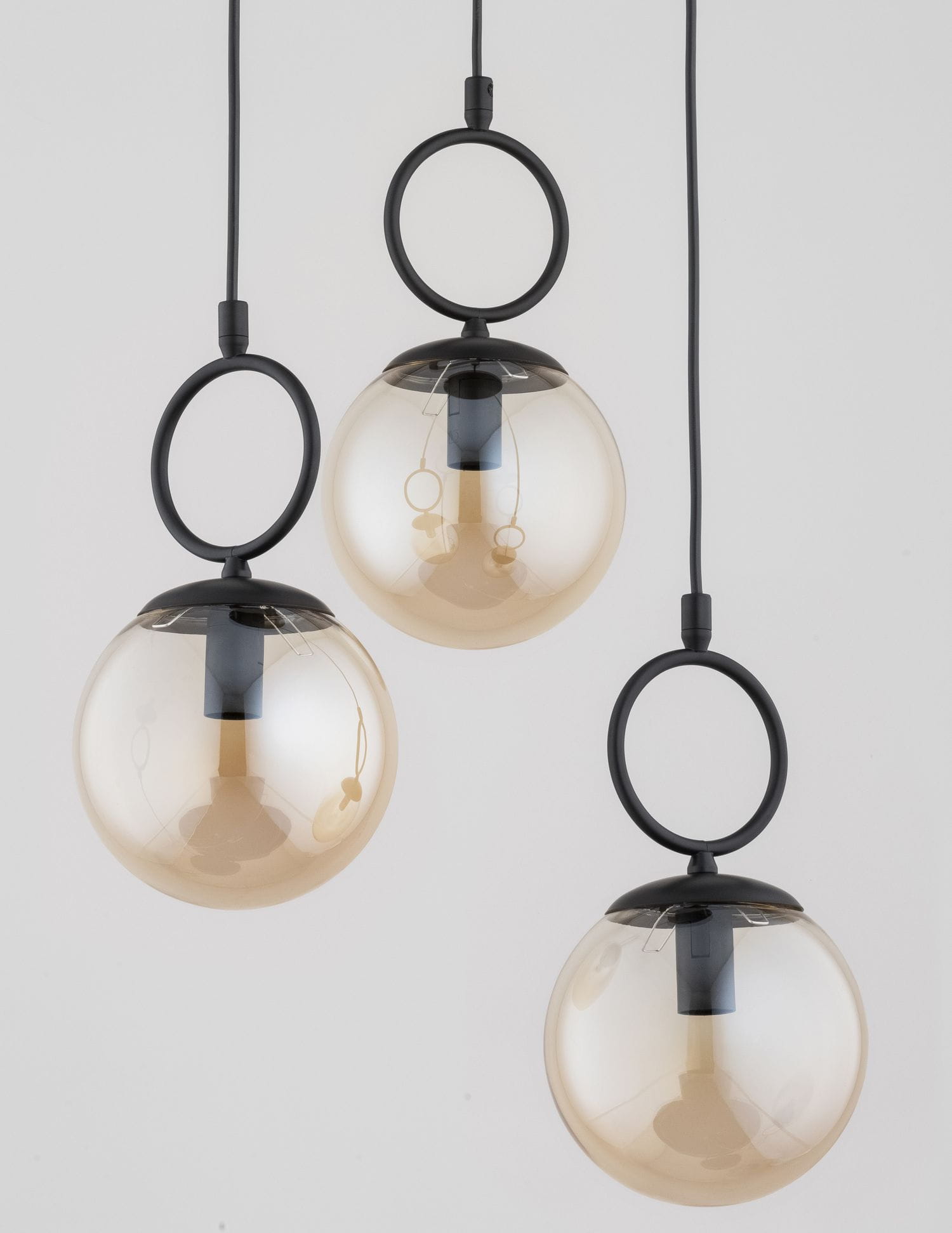Lampa wisząca Sitro z trzema kloszami E14 w kolorze czarnym i bursztynowym. Klosze w formie półprzezroczystych kul, zawieszone na czarnych linkach, z metalowymi okręgami. Produkt w pozycji wiszącej, na jednolitym tle.