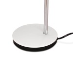 Biała lampka biurkowa Kajtek z podstawą okrągłą, metalową, na czarnym podłożu. Widoczny chromowany słup oraz kabel zasilający. Produkt przeznaczony do jednego źródła światła E27.