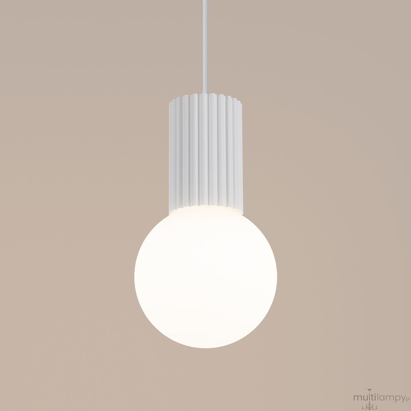 Biała lampa wisząca Halo z jedną oprawą G9. Okrągła, mlecznobiała kula z matowego szkła zawieszona na białym, tekstylnym przewodzie. Górna część lampy z żebrowanym wykończeniem. Tło w neutralnym odcieniu.