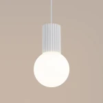 Biała lampa wisząca Halo z jedną oprawą G9. Okrągła, mlecznobiała kula z matowego szkła zawieszona na białym, tekstylnym przewodzie. Górna część lampy z żebrowanym wykończeniem. Tło w neutralnym odcieniu.