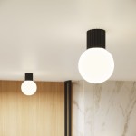 Czarna lampa sufitowa Halo z pojedynczym źródłem światła G9, o okrągłym, mlecznym kloszu. Ujęcie frontalne, lampa zamontowana na gładkim suficie, w tle widoczne elementy drewniane i marmurowe. Stylowa i nowoczesna forma.