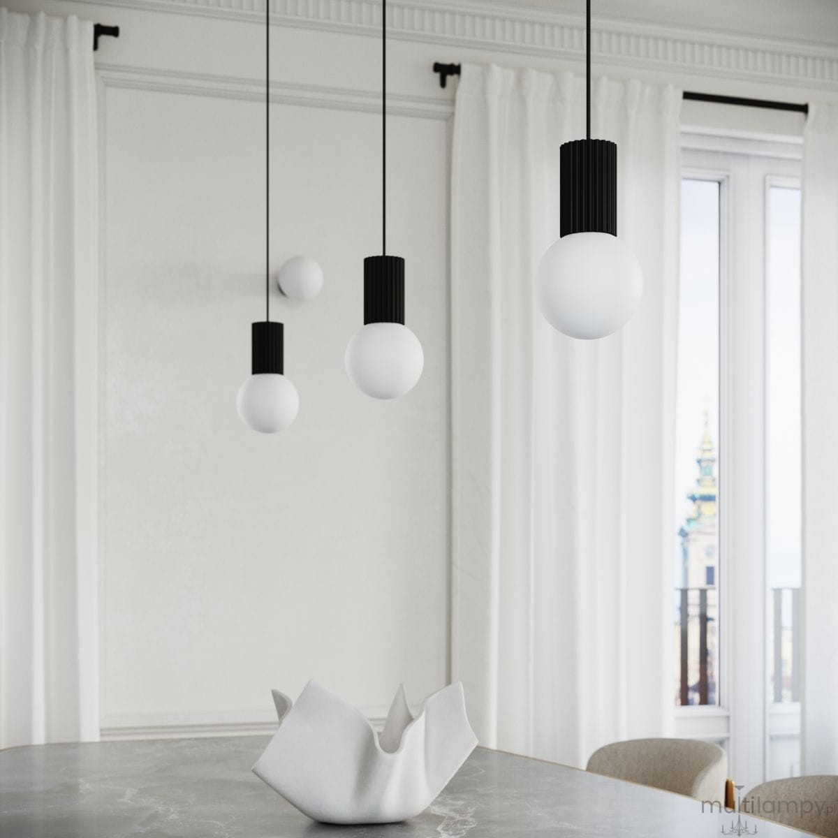 Czarna lampa wisząca Halo z jedną oprawą G9, z trzema kulistymi kloszami w białym kolorze, zawieszona na cienkich czarnych przewodach. Lampa w nowoczesnym stylu, umieszczona nad stołem, w jasnym wnętrzu z zasłonami.