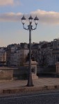 Lampa ogrodowa Vasco H235 w kolorze czarnym, stojąca, z trzema kloszami E27. Ujęcie frontalne, ukazujące ozdobny design i detalowe wykończenie. Tło to architektura miejskiego otoczenia, co podkreśla jej elegancki charakter.