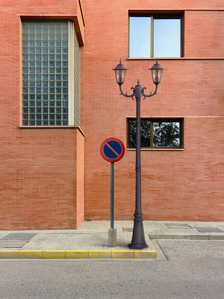 Lampa ogrodowa stojąca Standard H233 w kolorze czarnym z dwoma kloszami E27, ustawiona na chodniku obok znaku zakazu parkowania, z tłem w postaci czerwonej ceglanej ściany i dużych okien.