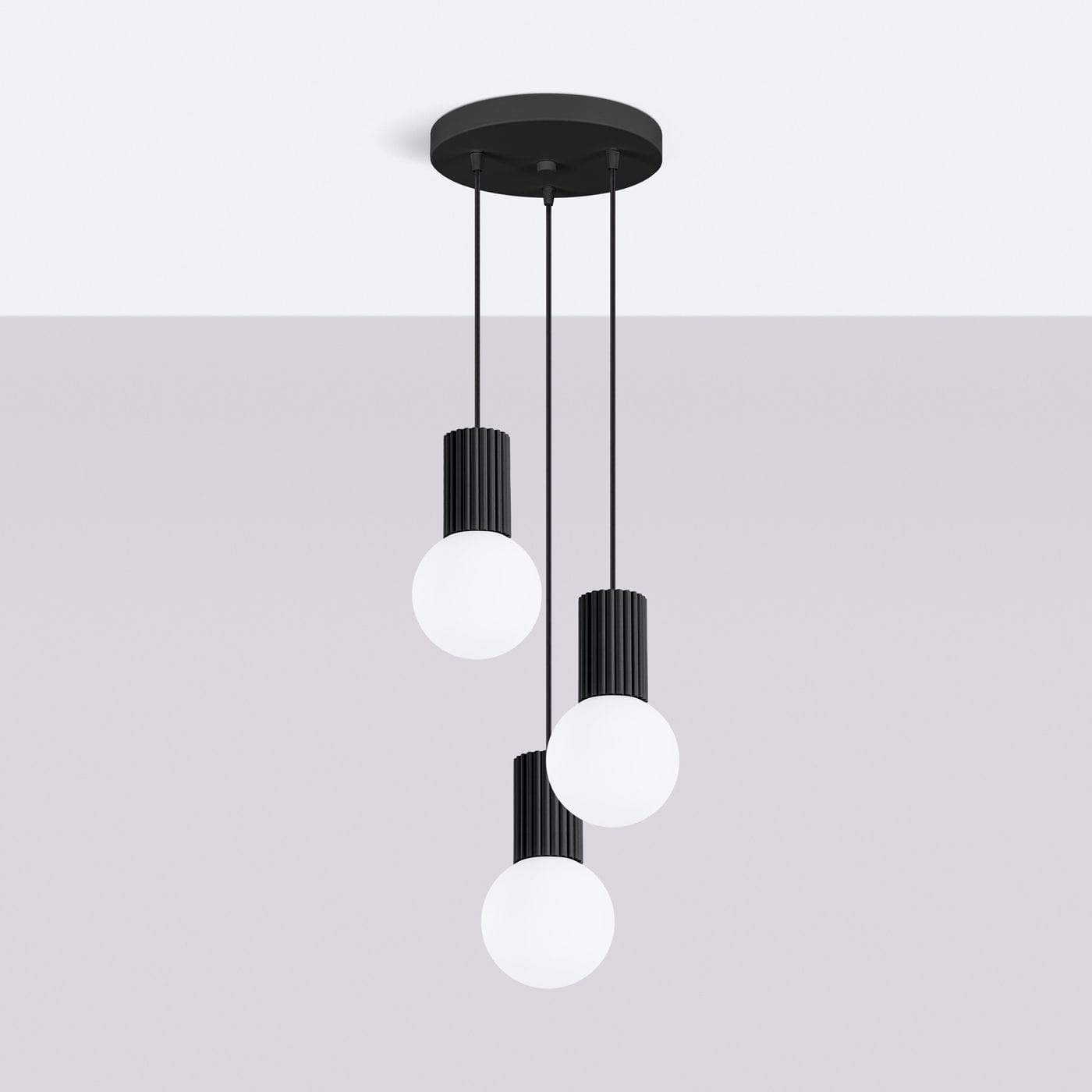 Lampa wisząca Halo 3xG9 w kolorze czarnym, z trzema okrągłymi, białymi kloszami na długich, cienkich linkach. Klosze osadzone w cylindrycznych, żebrowanych podstawach. Montaż sufitowy, minimalistyczny design na jasnym tle.