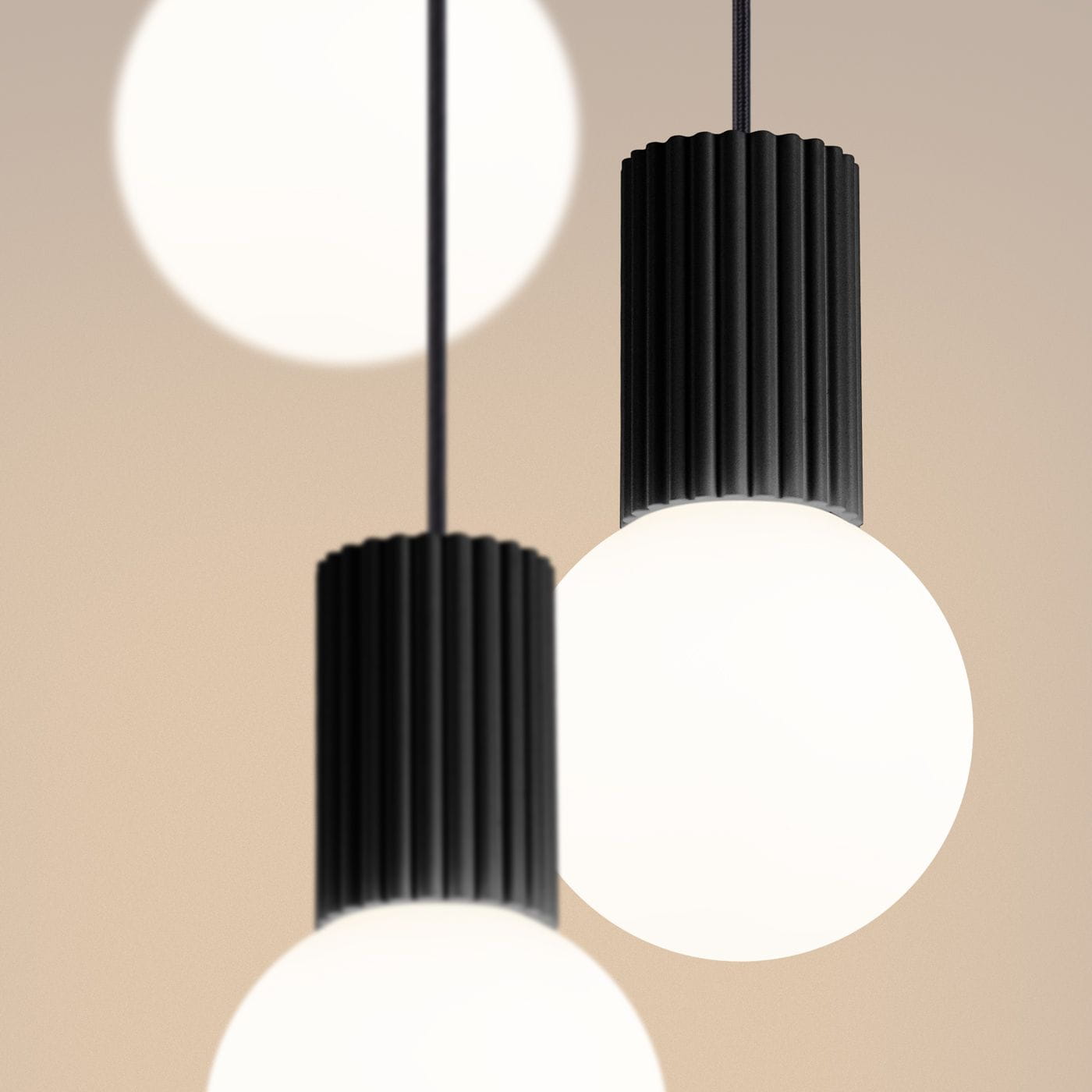 Lampa wisząca Halo 3xG9 w kolorze czarnym z cylindrycznymi, żebrowanymi oprawami i okrągłymi, białymi kloszami. Produkt zawieszony na czarnym przewodzie, w zbliżeniu na detale oprawy. Tło w neutralnym kolorze.