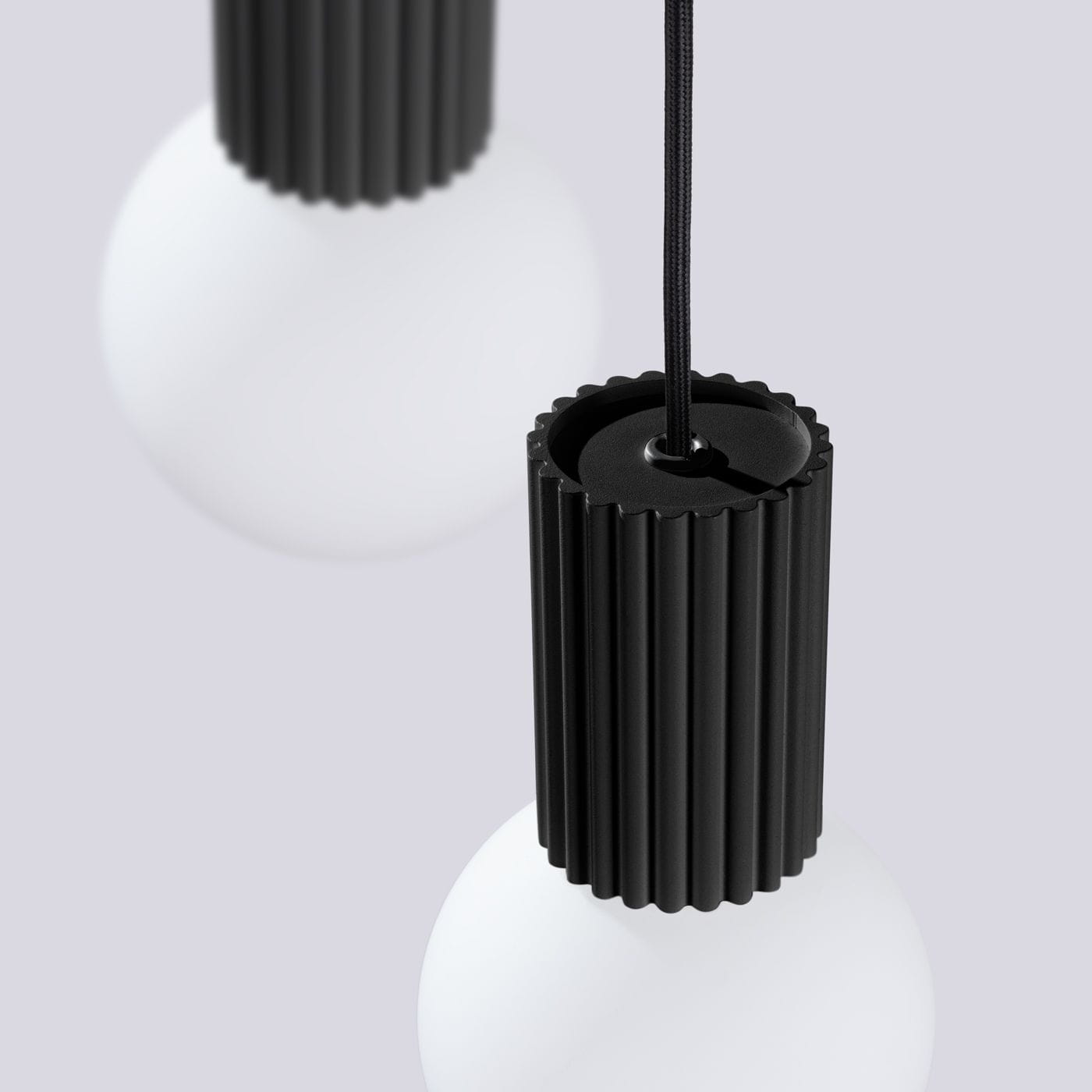 Czarna lampa wisząca Halo z trzema źródłami światła G9, z matową białą kulą i cylindrycznym, żłobkowanym uchwytem. Wisi na czarnym przewodzie, prezentując nowoczesny design. Tło w jasnym odcieniu szarości.