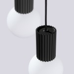 Czarna lampa wisząca Halo z trzema źródłami światła G9, z matową białą kulą i cylindrycznym, żłobkowanym uchwytem. Wisi na czarnym przewodzie, prezentując nowoczesny design. Tło w jasnym odcieniu szarości.