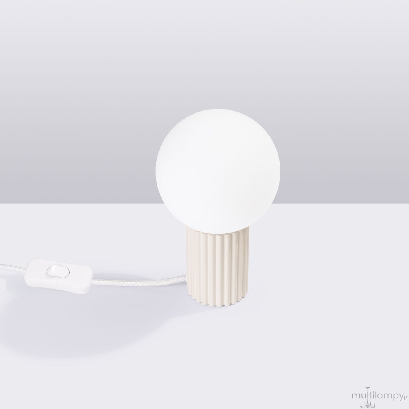 Beżowa lampa stołowa Halo z kulistym kloszem z białego szkła, umieszczona na cylindrycznej, żłobkowanej podstawie. Widoczny przełącznik w formie przycisku na przewodzie. Wysoka jakość materiałów, minimalistyczny design.