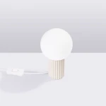 Beżowa lampa stołowa Halo z kulistym kloszem z białego szkła, umieszczona na cylindrycznej, żłobkowanej podstawie. Widoczny przełącznik w formie przycisku na przewodzie. Wysoka jakość materiałów, minimalistyczny design.