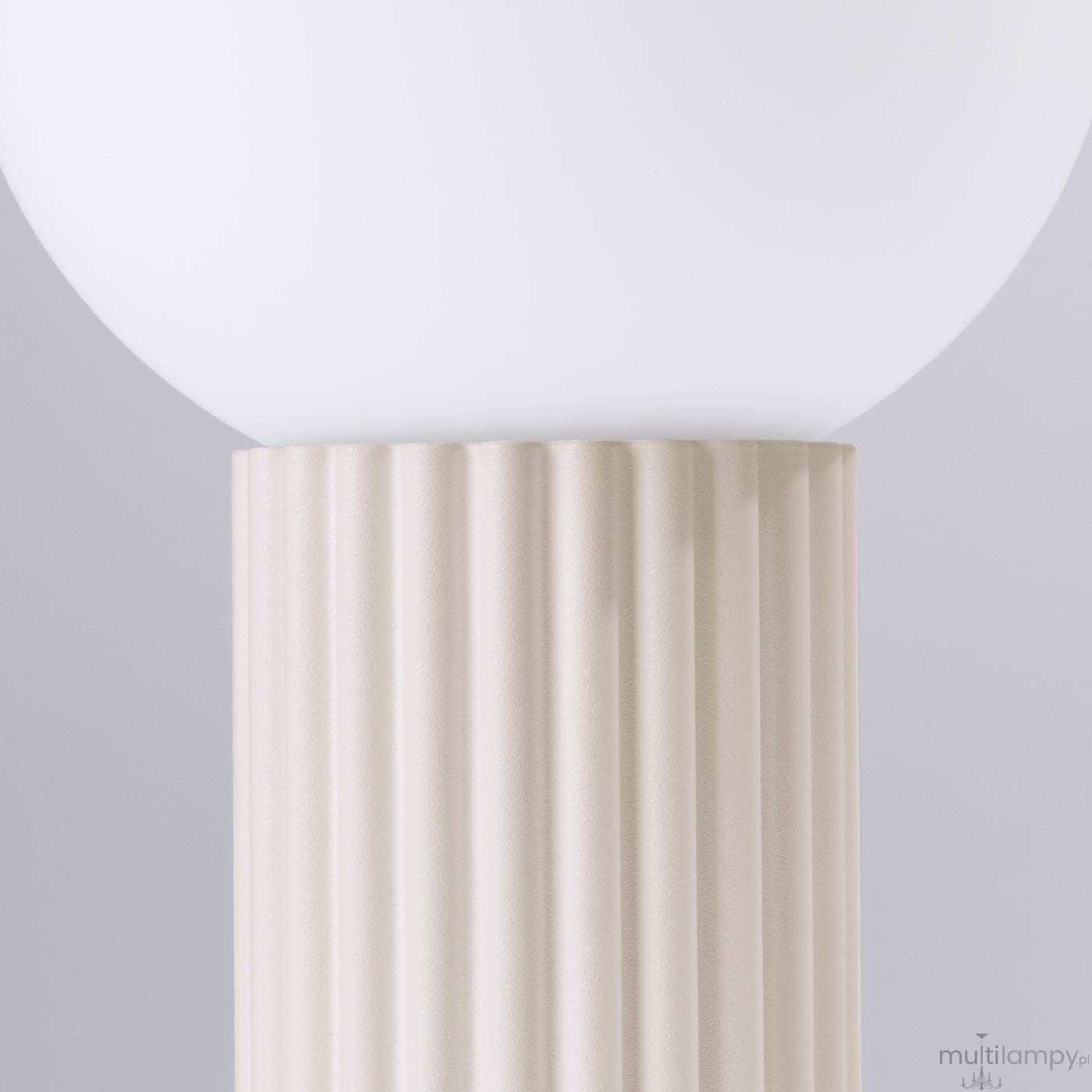 Beżowa lampa stołowa Halo z podstawą o żłobionej fakturze i okrągłym kloszem z białego szkła. Produkt widoczny z bliska, ukazujący detale podstawy oraz górną część z kloszem. Tło szare, neutralne.