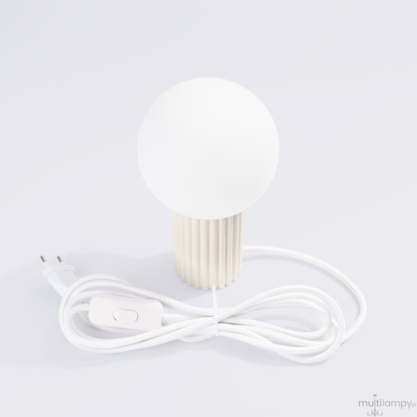 Beżowa lampa stołowa Halo z okrągłą, białą kloszem i żebrowanym stojakiem. Widoczny biały przewód z włącznikiem. Lampa z gniazdem na żarówkę G9, ustawiona na białym tle.
