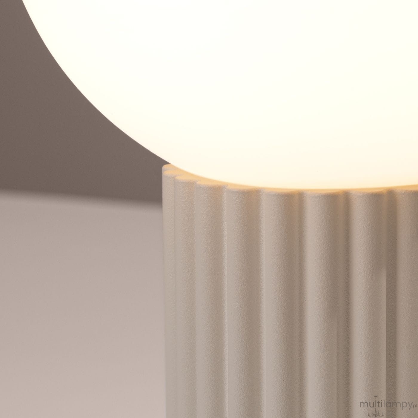 Beżowa lampa stołowa Halo z podstawą o teksturowanej, żłobkowanej powierzchni i okrągłym kloszem z mlecznego szkła. Ujęcie zbliżone na detal podstawy i klosza, podkreślające subtelny design.
