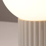 Beżowa lampa stołowa Halo z podstawą o teksturowanej, żłobkowanej powierzchni i okrągłym kloszem z mlecznego szkła. Ujęcie zbliżone na detal podstawy i klosza, podkreślające subtelny design.