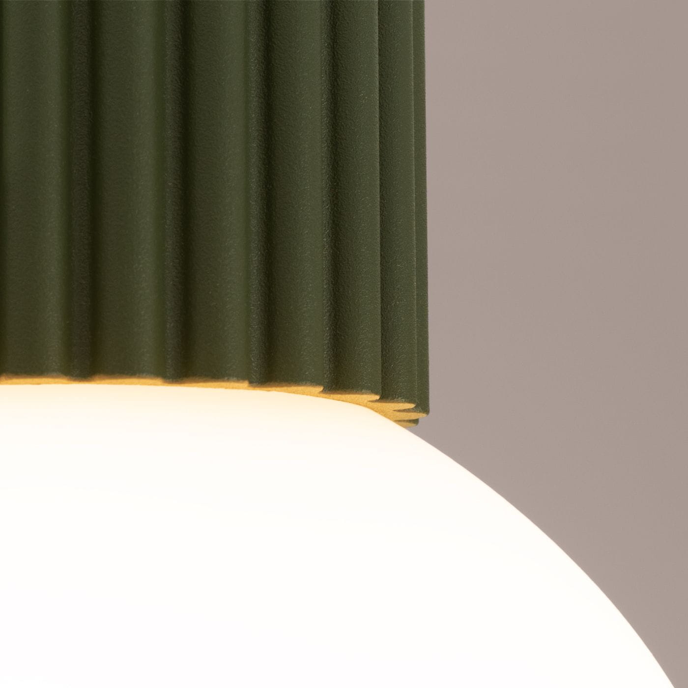 Lampa sufitowa w kolorze oliwkowej zieleni z żebrowanym kloszem, z białym, okrągłym źródłem światła. Widok zbliżony na detale górnej części lampy, ukazujący teksturę i kształt. Produkt przeznaczony do użytku wewnętrznego, posiada stopień ochrony IP44.