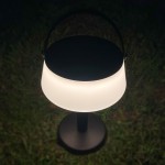Czarna lampa stołowa solarna LED Aure o mocy 2,2W, z białym kloszem w kształcie półkuli. Ujęcie z góry, stojąca na trawie. Oświetlenie o temperaturze barwowej 2700K, klasyfikacja IP44, odporna na warunki atmosferyczne.