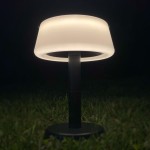 Lampa stołowa solarna LED Aure o mocy 2,2W, kolor czarny. Posiada okrągłą, białą klosz, umieszczoną na prostym słupku. Widok z dołu, na tle trawy, podkreślający subtelne oświetlenie. Klasa szczelności IP44 zapewnia odporność na warunki atmosferyczne.