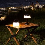 Czarna lampa stołowa solarna LED Aure o mocy 2,2W i barwie światła 2700K, umieszczona na drewnianym stole. Lampa ma minimalistyczny design z okrągłym kloszem i metalową podstawą, obok niej druga lampa w formie przenośnej.