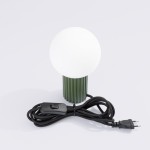 Lampa stołowa Halo 1xG9 w kolorze oliwkowej zieleni, z białą, okrągłą kloszem. Ustawiona w pionie, z widocznym czarnym kablem z przełącznikiem. Dół lampy ma teksturowaną, żebrowaną strukturę.