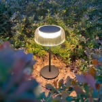 Czarna lampa stołowa solarna LED Bluet 2,5W z kloszem o żebrowanej fakturze, emitująca ciepłe światło 3000K. Ustawiona na tle zieleni, z metalową podstawą i widocznym panelem słonecznym na górze.