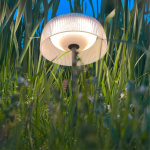 Czarna lampa stołowa solarna LED Bluet 2,5W z kloszem o fakturze prążkowanej, umieszczona w trawie, emituje ciepłe światło (3000K). Stojąca, z prostym stelażem, odporna na warunki atmosferyczne (IP44).