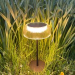 Czarna lampa stołowa solarna LED Bluet 2,5W 3000K IP44 z przezroczystym kloszem, umieszczona na zielonej trawie. Klosz z pionowymi żłobieniami, emitujący ciepłe światło, na prostym, okrągłym stelażu.