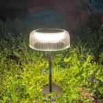 Czarna lampa stołowa solarna LED Bluet z kloszem o fakturze żłobkowanej, emitująca ciepłe światło 3000K. Ustawiona na zielonej trawie, z widocznym metalowym stelażem i podstawą. Wysokość lampy wynosi około 30 cm.
